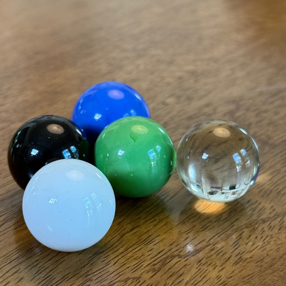 Five marbles, blue, green, clear, white, black. 1" diameter on a wood table